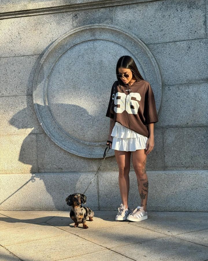 menina com camiseta oversized e saia segurando um cachorro